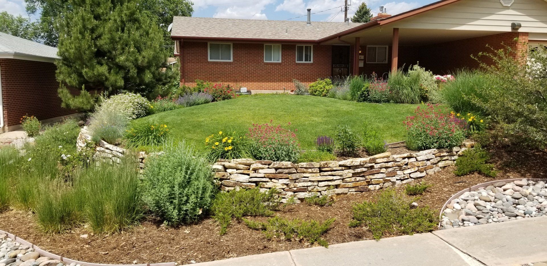 A house with a terraced yard, stone wall, and colorful flowering plants.