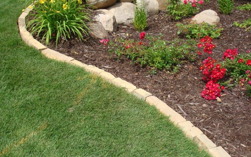 Lawn with a brick border separating green grass from a garden bed with flowers and mulch.