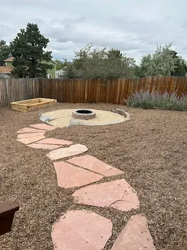 Backyard with red stone path, fire pit, raised garden bed, and wood chip ground cover.