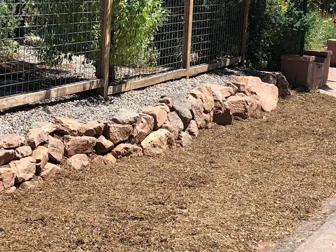 Stone retaining wall with wood chip mulch and a wire fence.