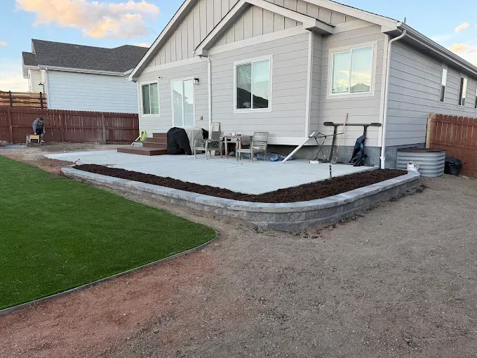 Concrete patio bordered by retaining wall, adjacent to artificial grass, backyard setting.