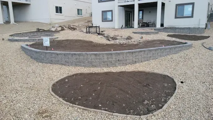 Landscaped yard with retaining walls, gravel, and dirt patches in front of a house.