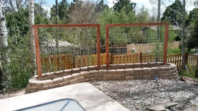 Raised garden bed with trellis, constructed of brick and wood, in a backyard setting.