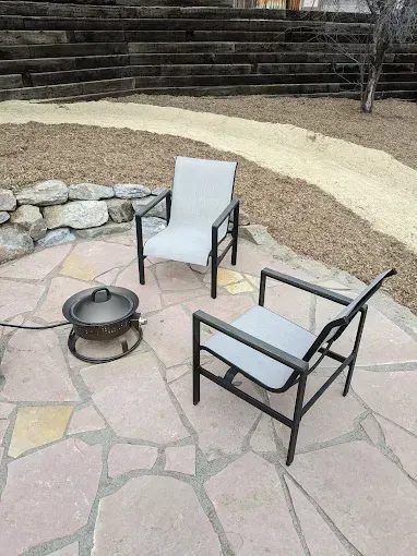 Two chairs and a fire pit on a stone patio; gravel path and stone steps in the background.