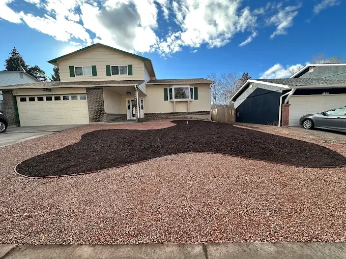 Beige house with a gravel yard and a dark mulch bed; blue sky.