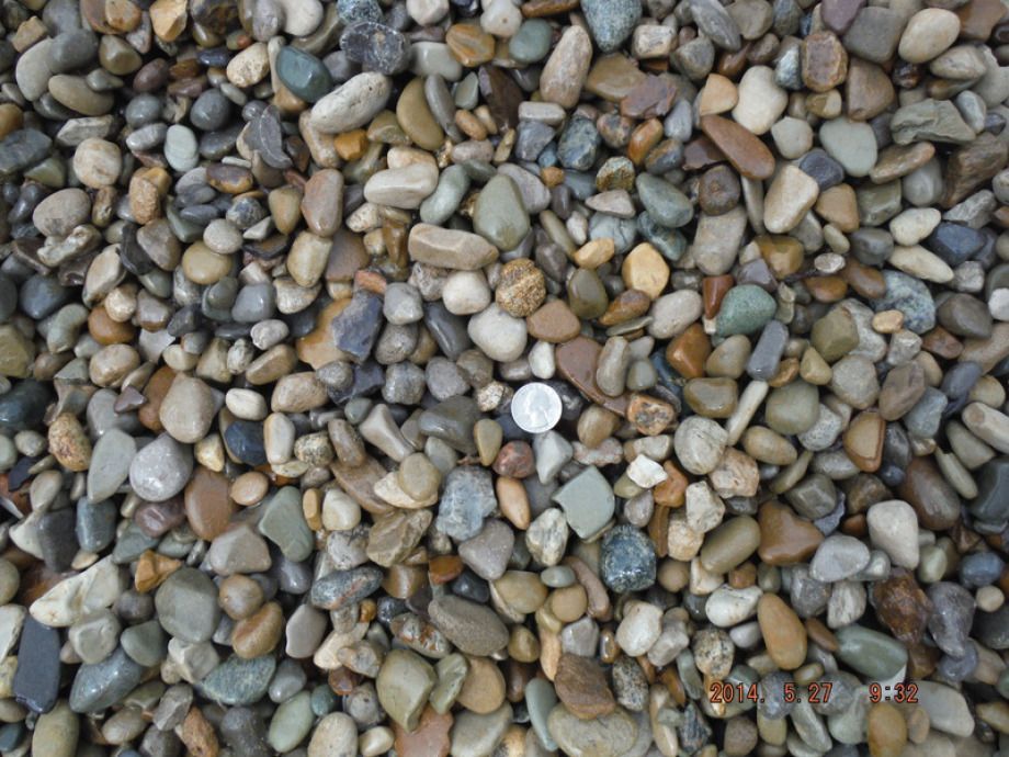 Smooth, multi-colored river rocks, with a silver coin for scale, scattered on a surface.