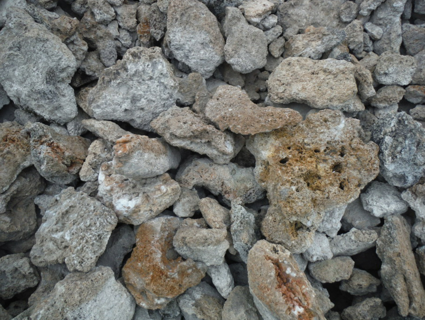 Pile of porous, light-colored rocks. Some are grey, tan, or have orange-brown patches.