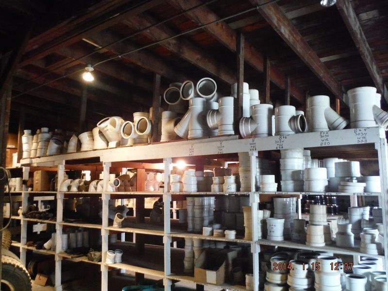 Shelves filled with white plumbing pipes and fittings in a dimly lit warehouse.