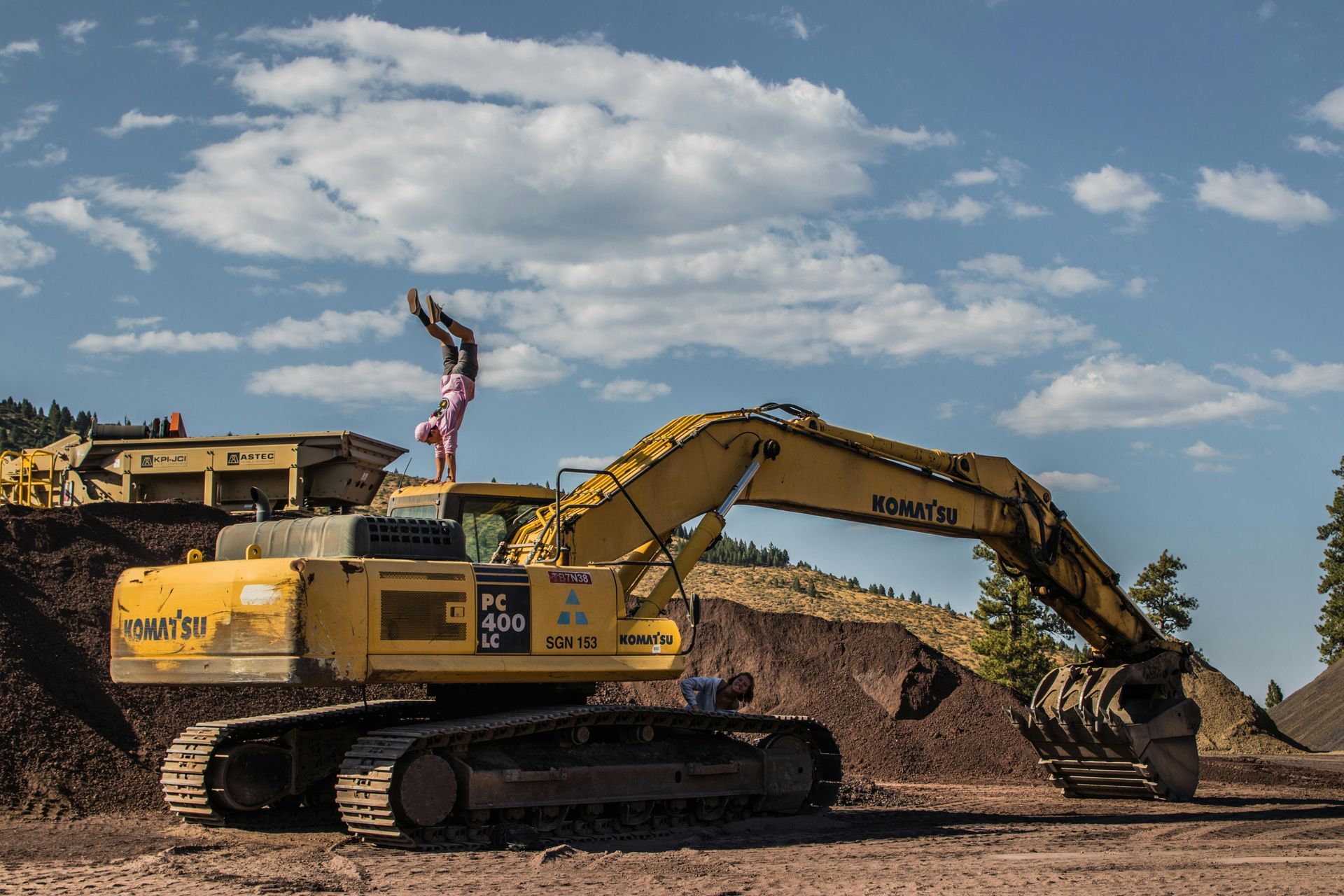 Person doing a handstand on a yellow excavator in a construction site under a blue sky.