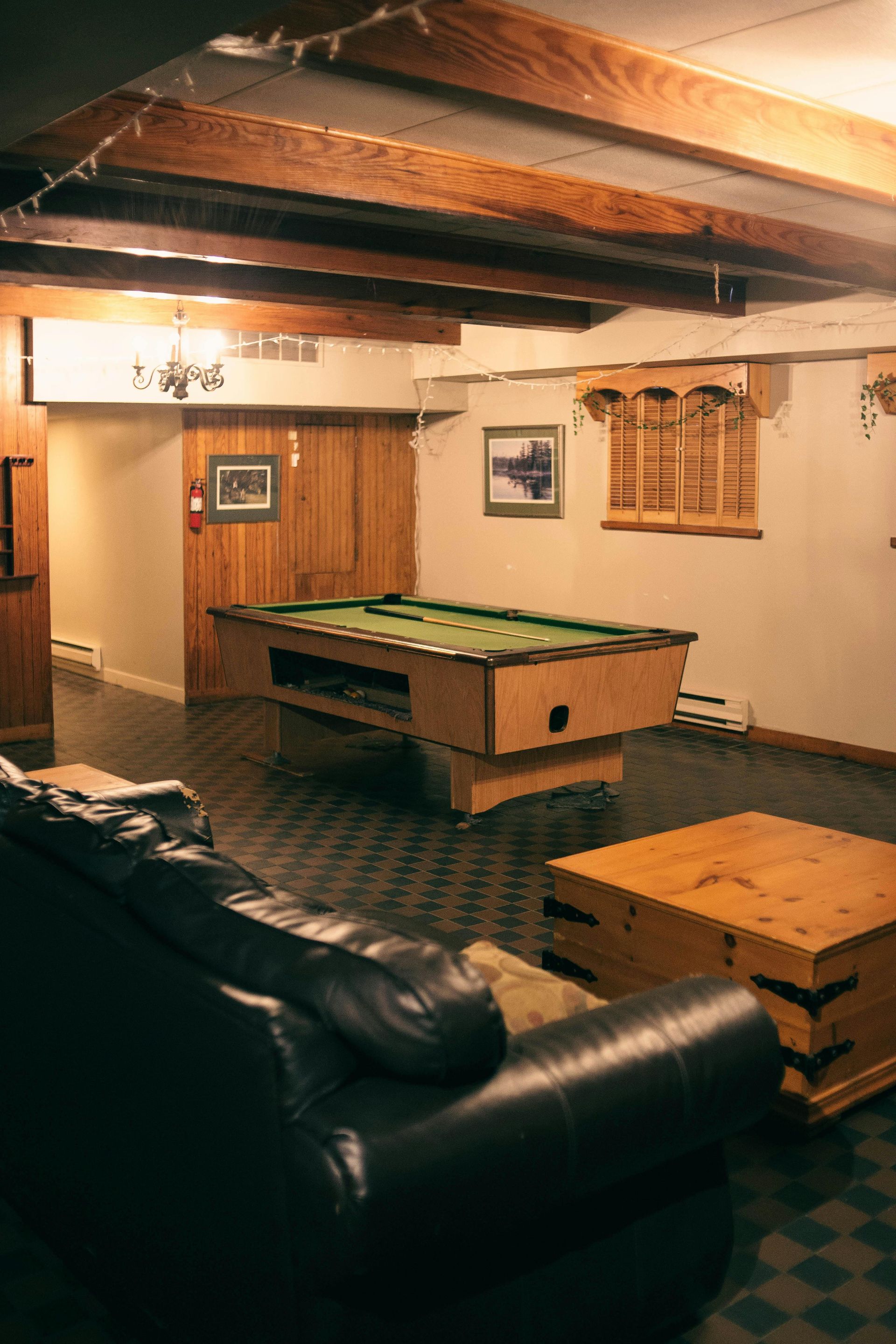 Basement with pool table, leather couch, wooden beams and chest, and artwork.