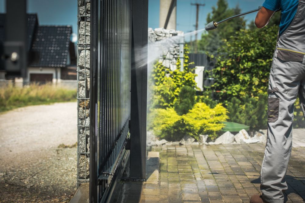 A Man is Cleaning a Fence With a High Pressure Washer — SOAKD Exterior Cleaning in Kariong, NSW