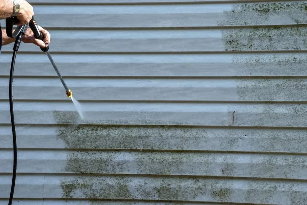 A person is cleaning a siding with a high pressure washer.— Soakd In Kariong, NSW