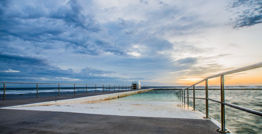 Ocean Pool With White Edges, Metal Railings, and Cloudy Sky at Sunset — SOAKD Exterior Cleaning in Merewether, NSW