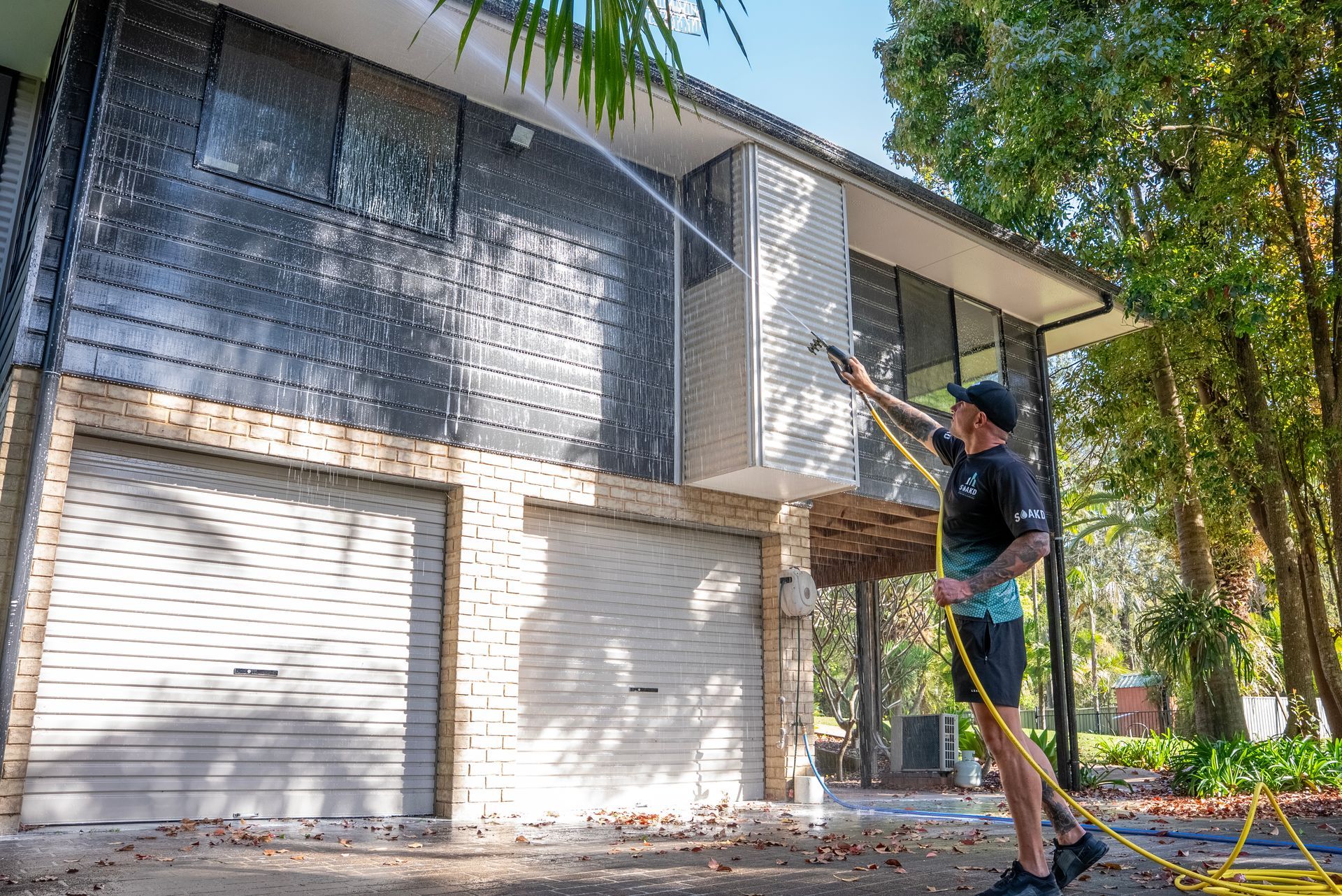 A Man is Using a High Pressure Washer to Clean a Wall — SOAKD Exterior Cleaning in Central Coast, NSW