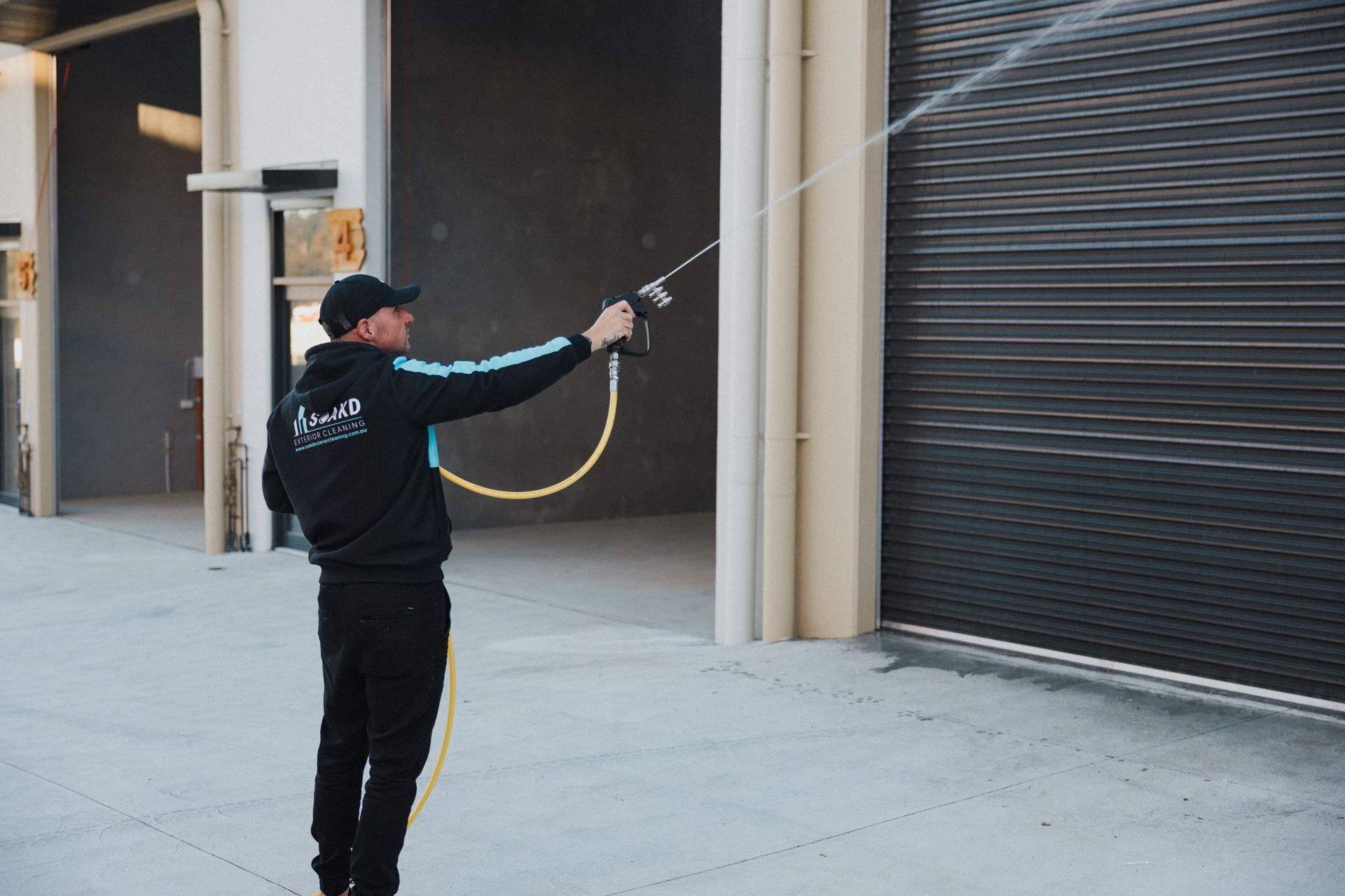 A person is cleaning the side of a house with a high pressure washer. — Soakd In Kariong, NSW