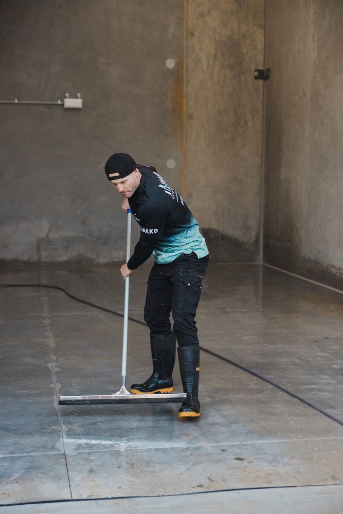 Man in Work Clothes Squeegees a Concrete Floor — SOAKD Exterior Cleaning in Adamstown, NSW