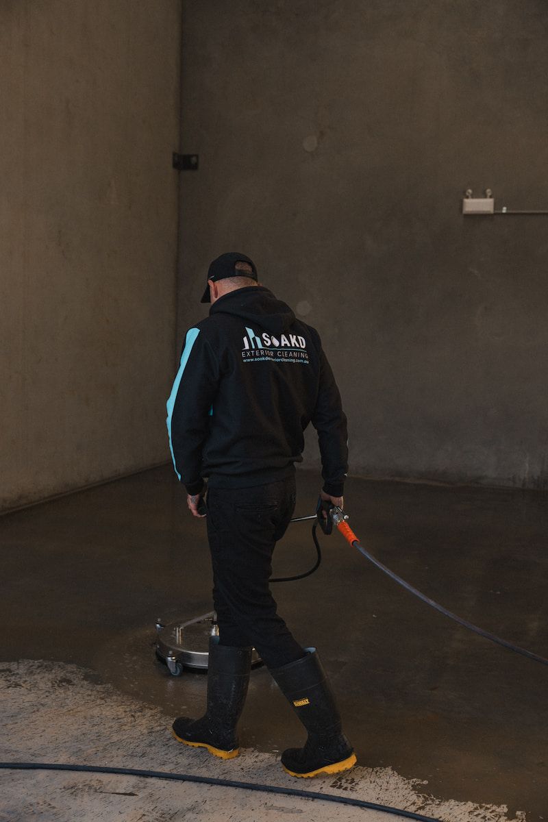 A Man Pressure Washing a Concrete Floor — SOAKD Exterior Cleaning in Lambton, NSW