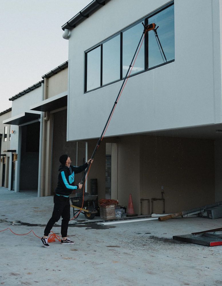 A Man is Using a High Pressure Washer to Clean a Wall — SOAKD Exterior Cleaning in Kariong, NSW