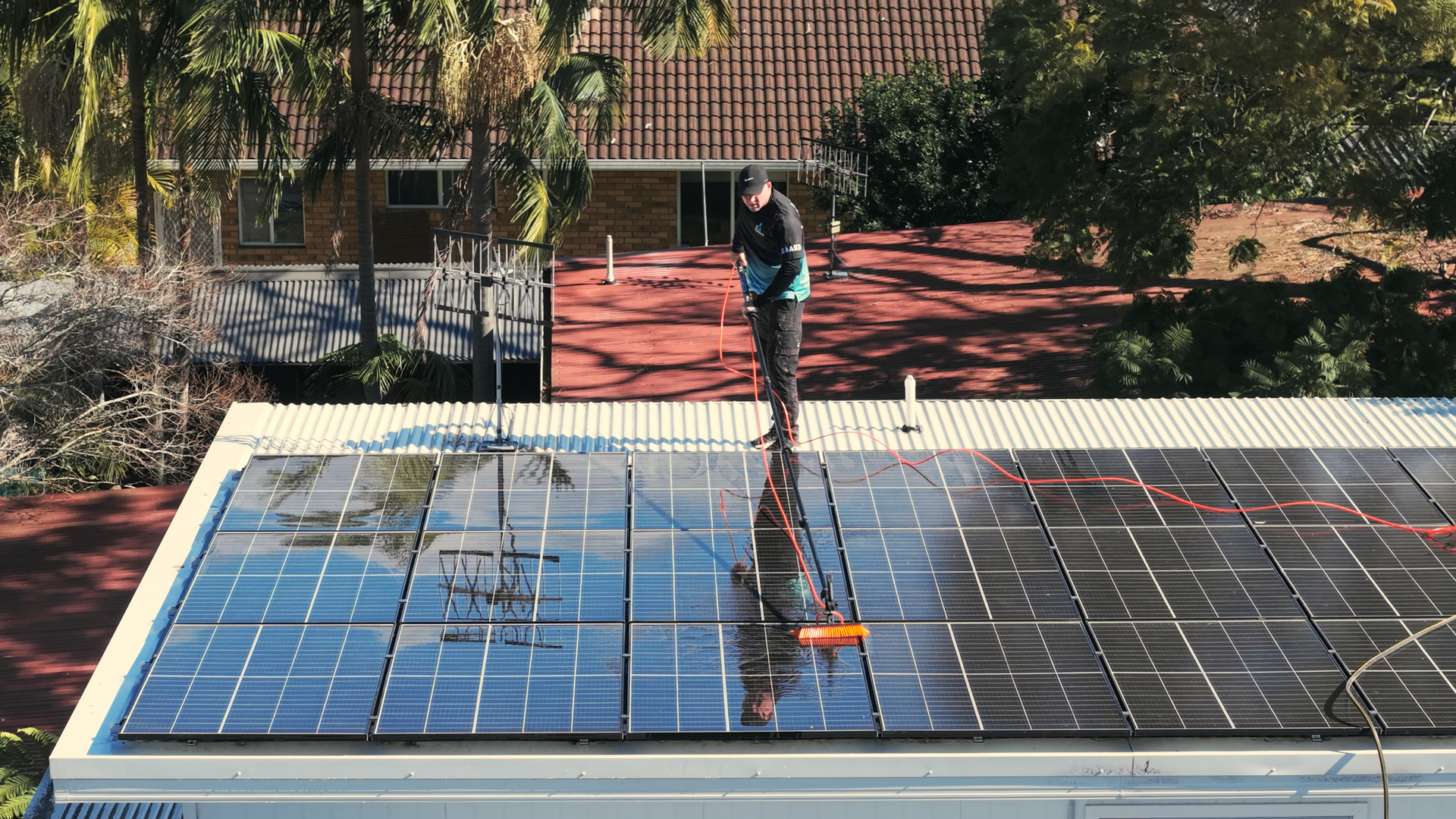 A Person is Cleaning Solar Panels on a Roof With a High Pressure Washer — SOAKD Exterior Cleaning in Central Coast, NSW