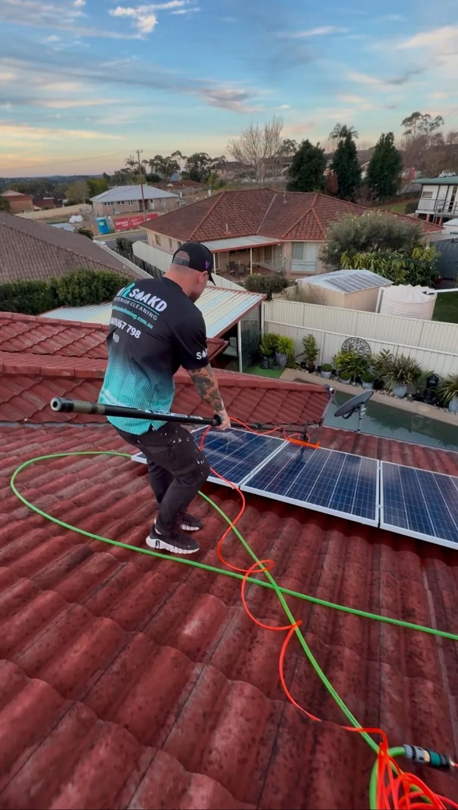 A Man is Cleaning Solar Panels on the Roof of a House — SOAKD Exterior Cleaning in Kariong, NSW