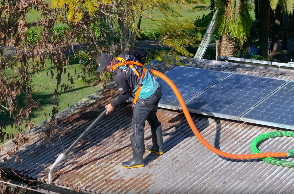 Person cleaning a corrugated metal roof with solar panels. They wear a harness, using a hose. — SOAKD Exterior Cleaning in Central Coast, NSW