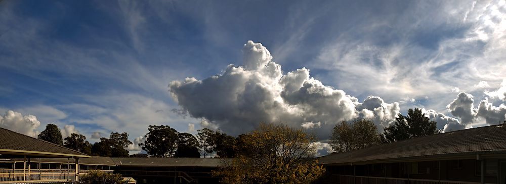 Clouds in a Blue Sky Above Buildings With Trees — SOAKD Exterior Cleaning in Matcham, NSW