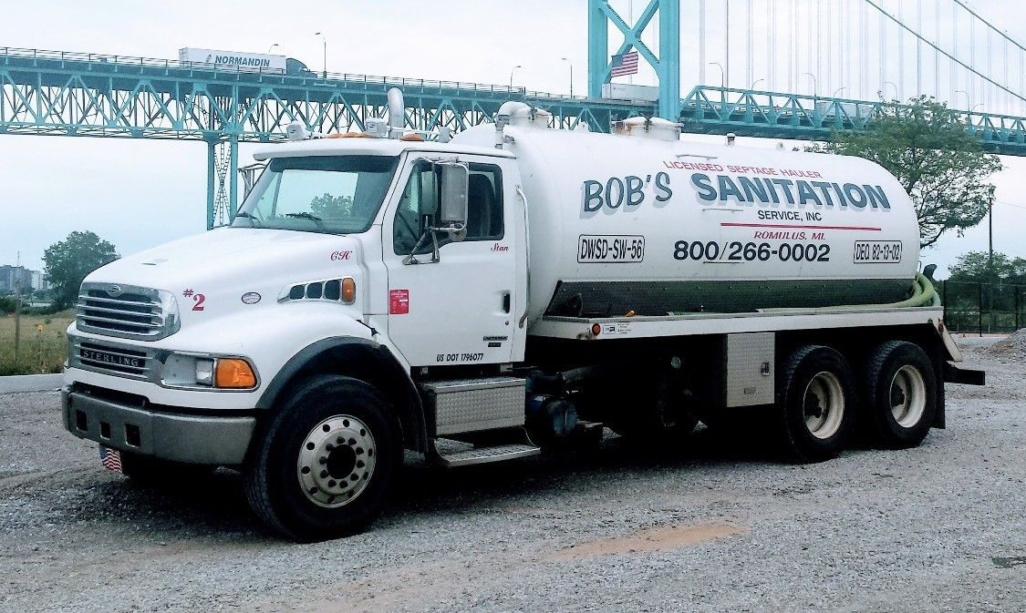 Concrete rectangular structure in ground, filled with mulch. Grey walls. Black object in the middle. Spade in foreground.