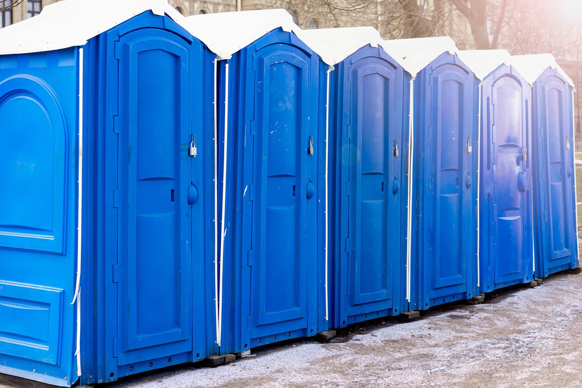 Row of blue portable toilets outdoors on a paved surface.