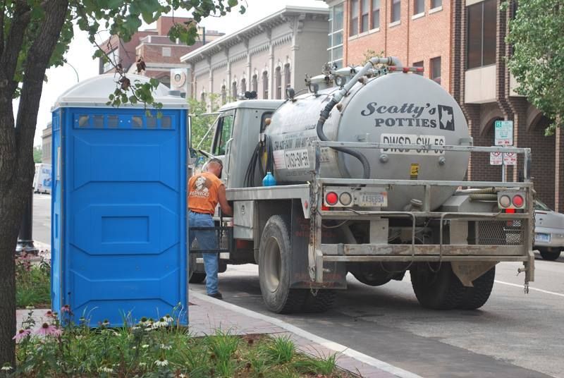 White portable restroom trailer on a tarmac with stairs and ramp for access. Aircraft visible in the background. White portable restroom trailer on a tarmac with stairs and ramp for access. Aircraft visible in the background.