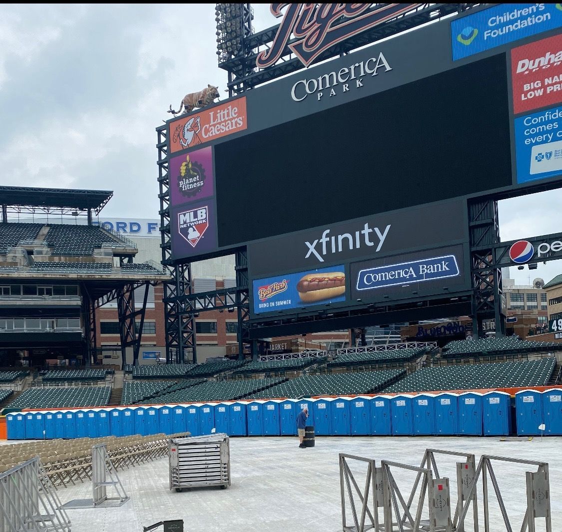 Man entering a blue portable toilet, carrying a backpack. Outdoors, sunlight. Man entering a blue portable toilet, carrying a backpack. Outdoors, sunlight.