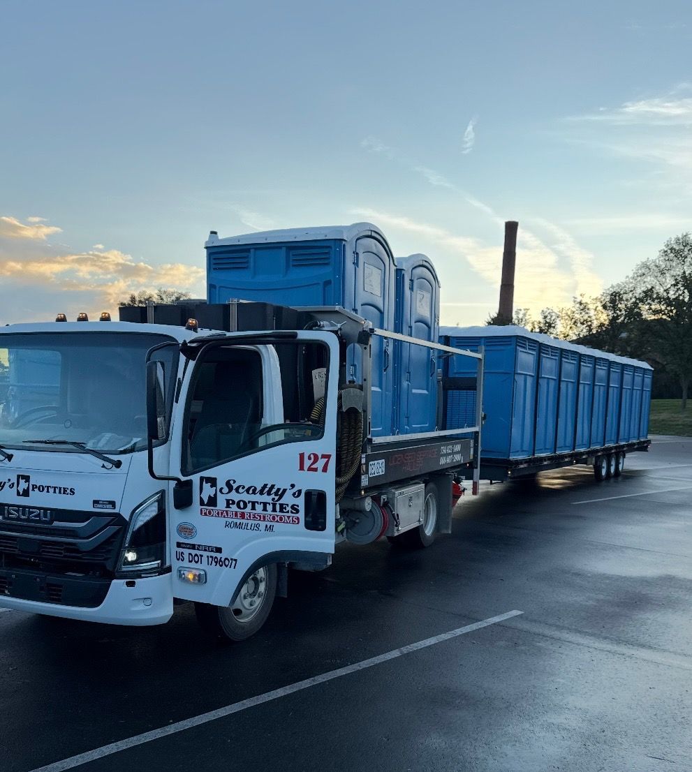 Two portable toilets, one blue and one gray, outdoors in a grassy area with trees. One door is open. Two portable toilets, one blue and one gray, outdoors in a grassy area with trees. One door is open.