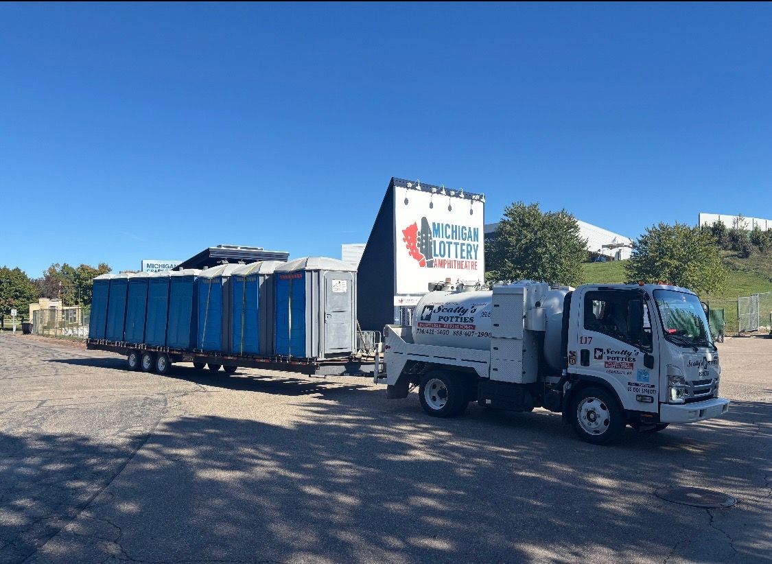 Row of blue portable toilets with yellow roofs on a paved surface. Cloudy sky and grassy area in the background. Row of blue portable toilets with yellow roofs on a paved surface. Cloudy sky and grassy area in the background.