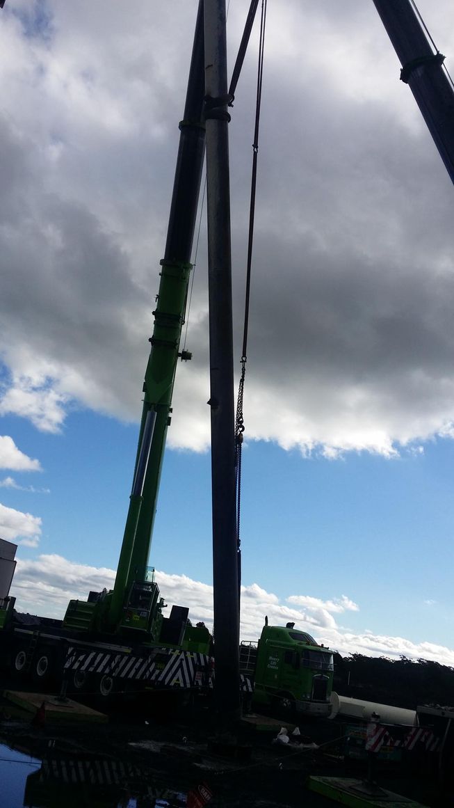 a green crane is lifting a large pole in the sky