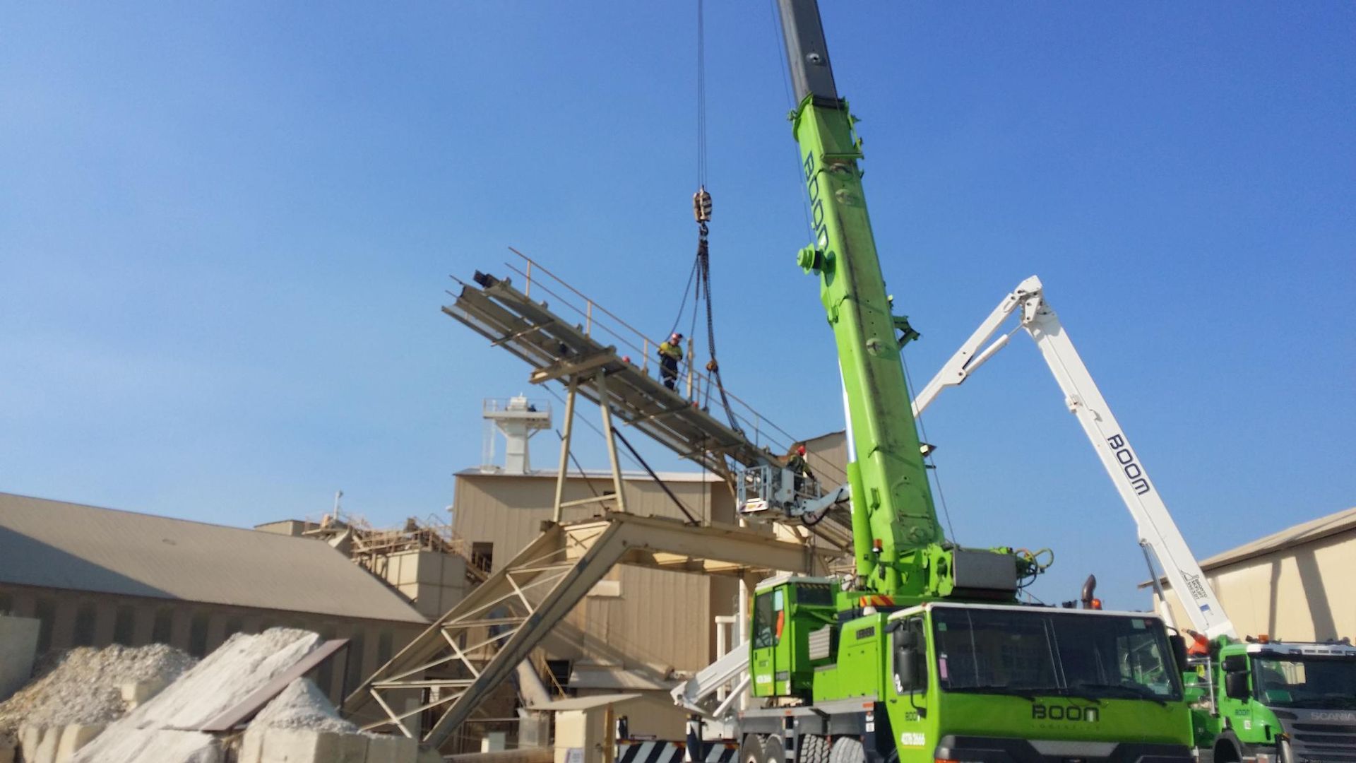 a green crane is lifting a piece of metal in front of a building .