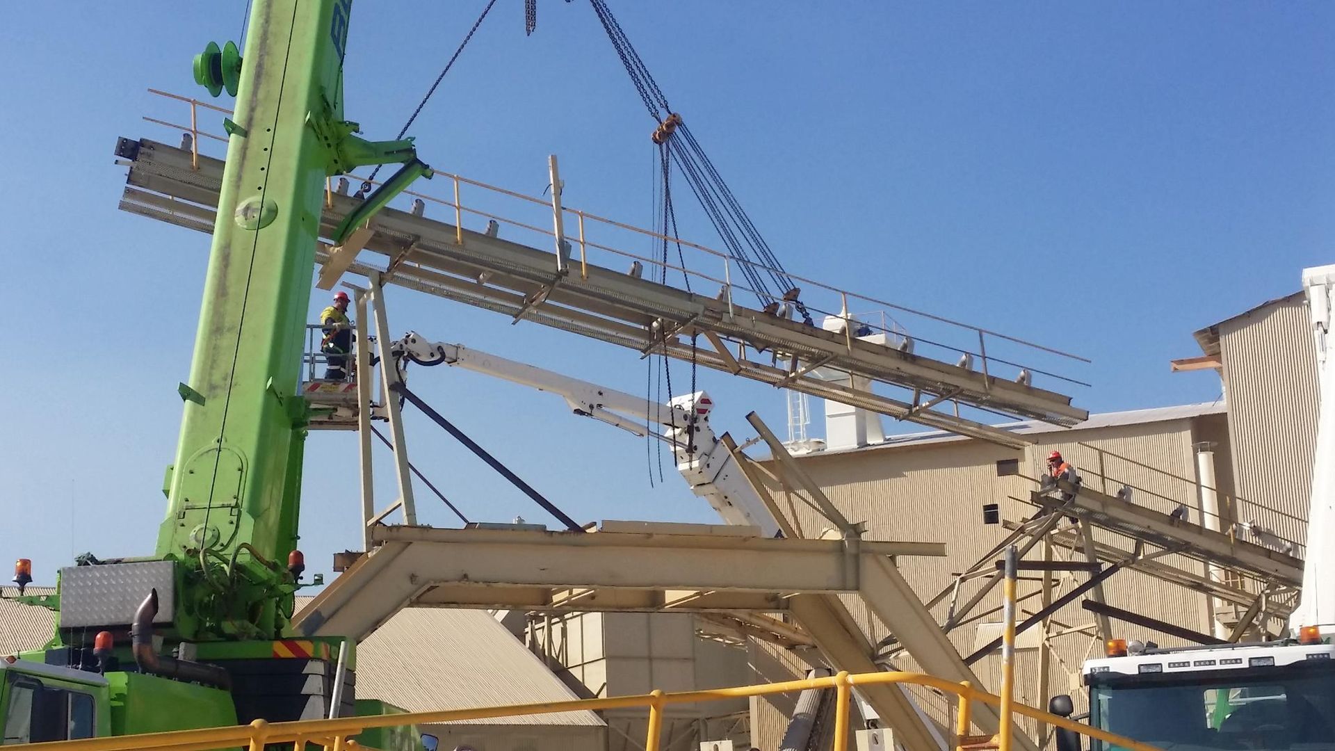 a green crane is lifting a metal structure in front of a building