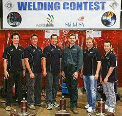 a group of men are standing in front of a welding contest sign .