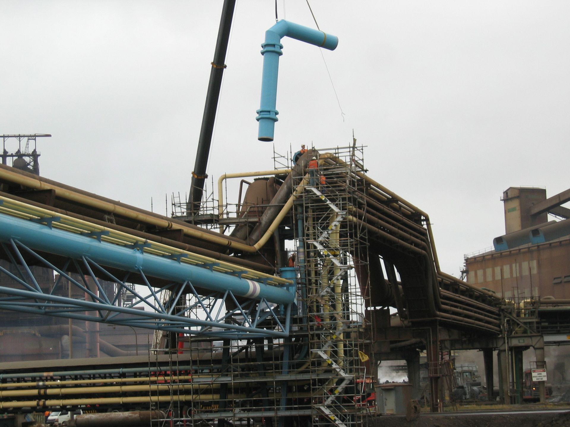 a blue pipe is being lifted by a crane in a factory