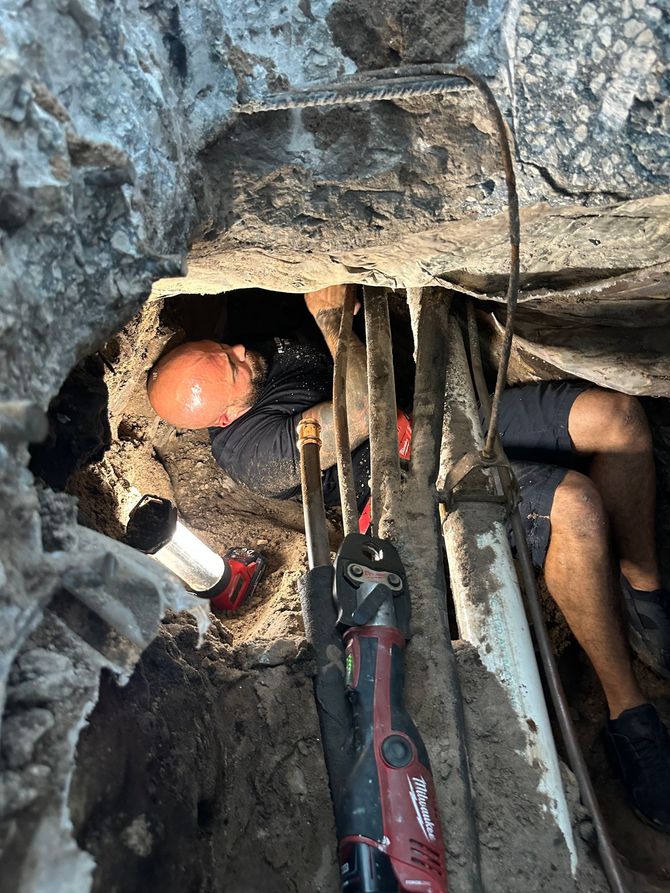 A man is working on a pipe in a hole in the ground.