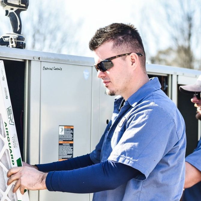 A man wearing sunglasses is working on an air conditioner