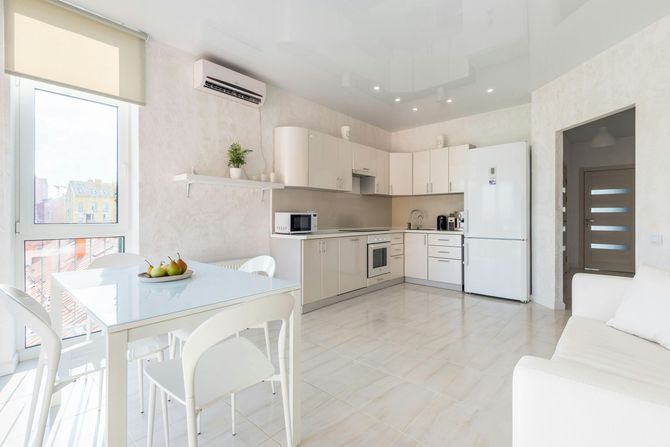 A kitchen with white cabinets , a refrigerator , a table and chairs.
