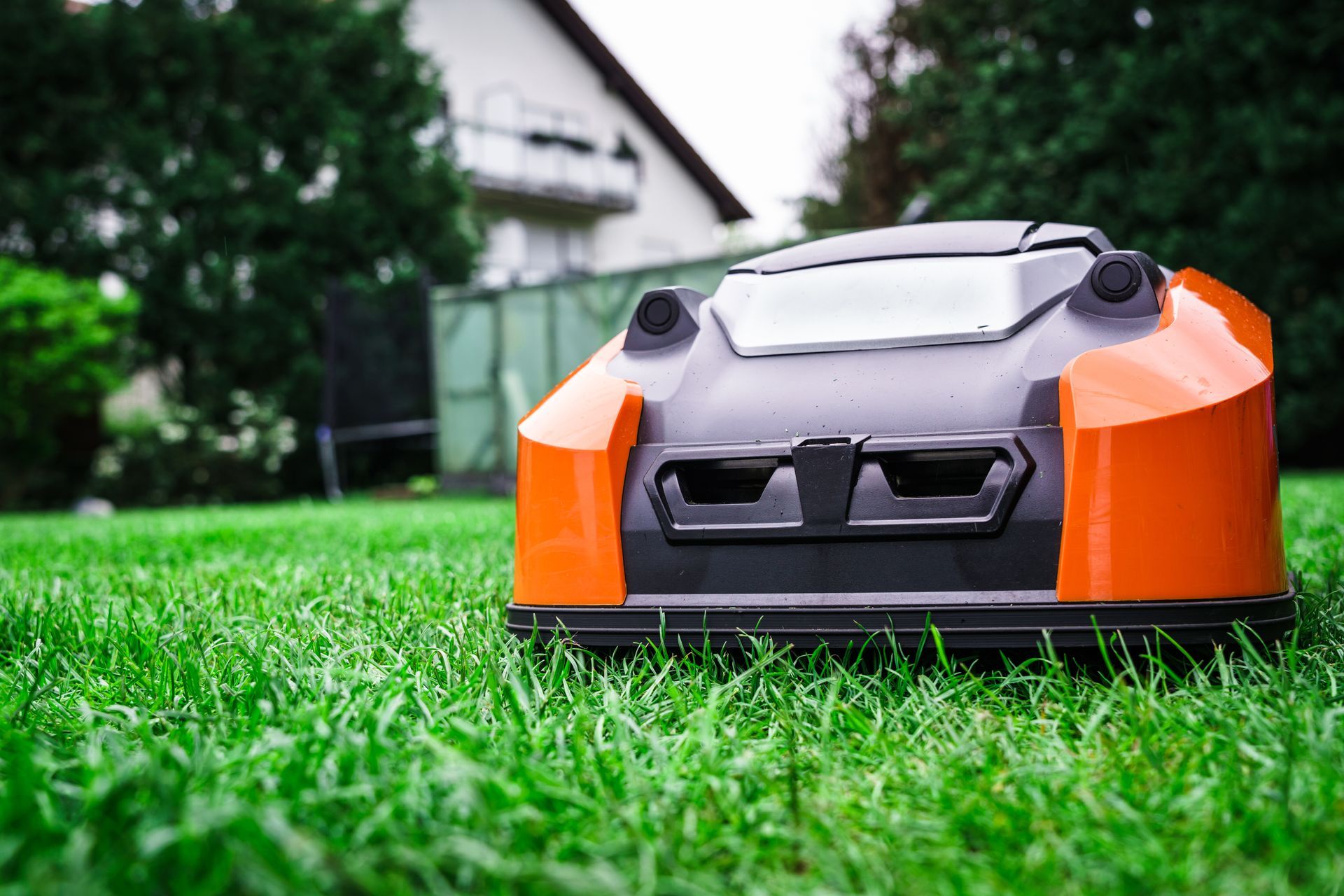 An orange and black robotic lawnmower sits on a green, freshly cut lawn in front of a house.