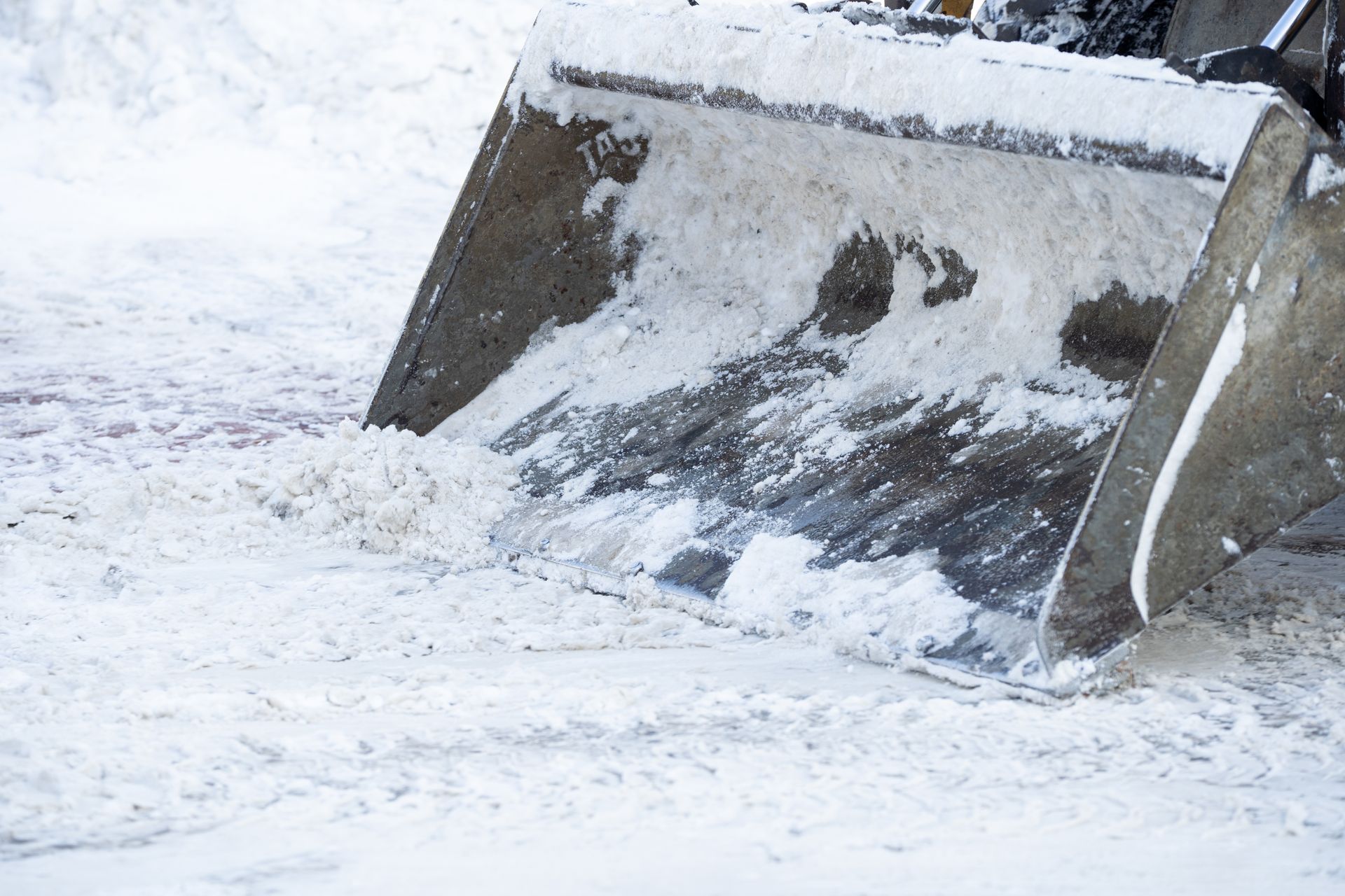 A close-up view of a metal snowplow blade pushing through deep snow on a winter day.