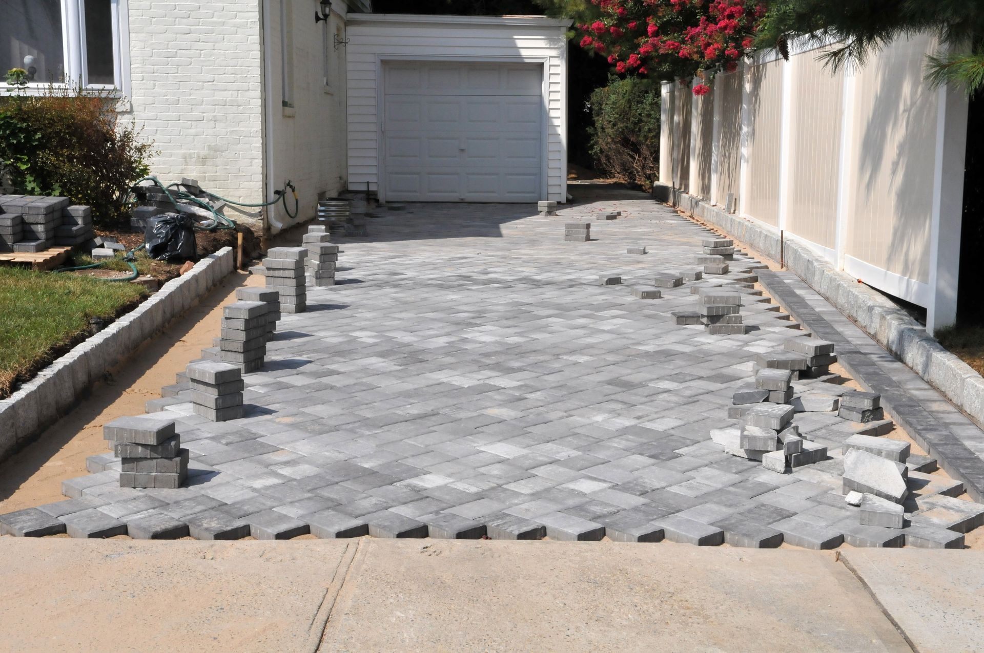 A residential driveway under construction, featuring a newly laid gray herringbone paver pattern leading to a garage.