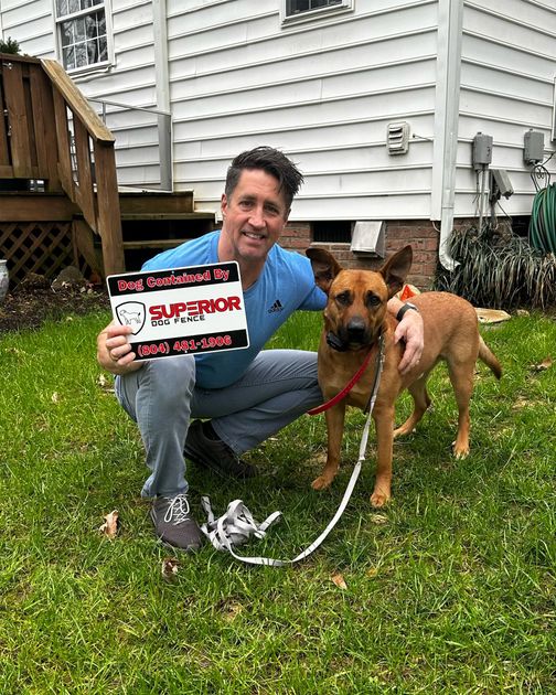 A man is kneeling down next to a dog on a leash and holding a sign.