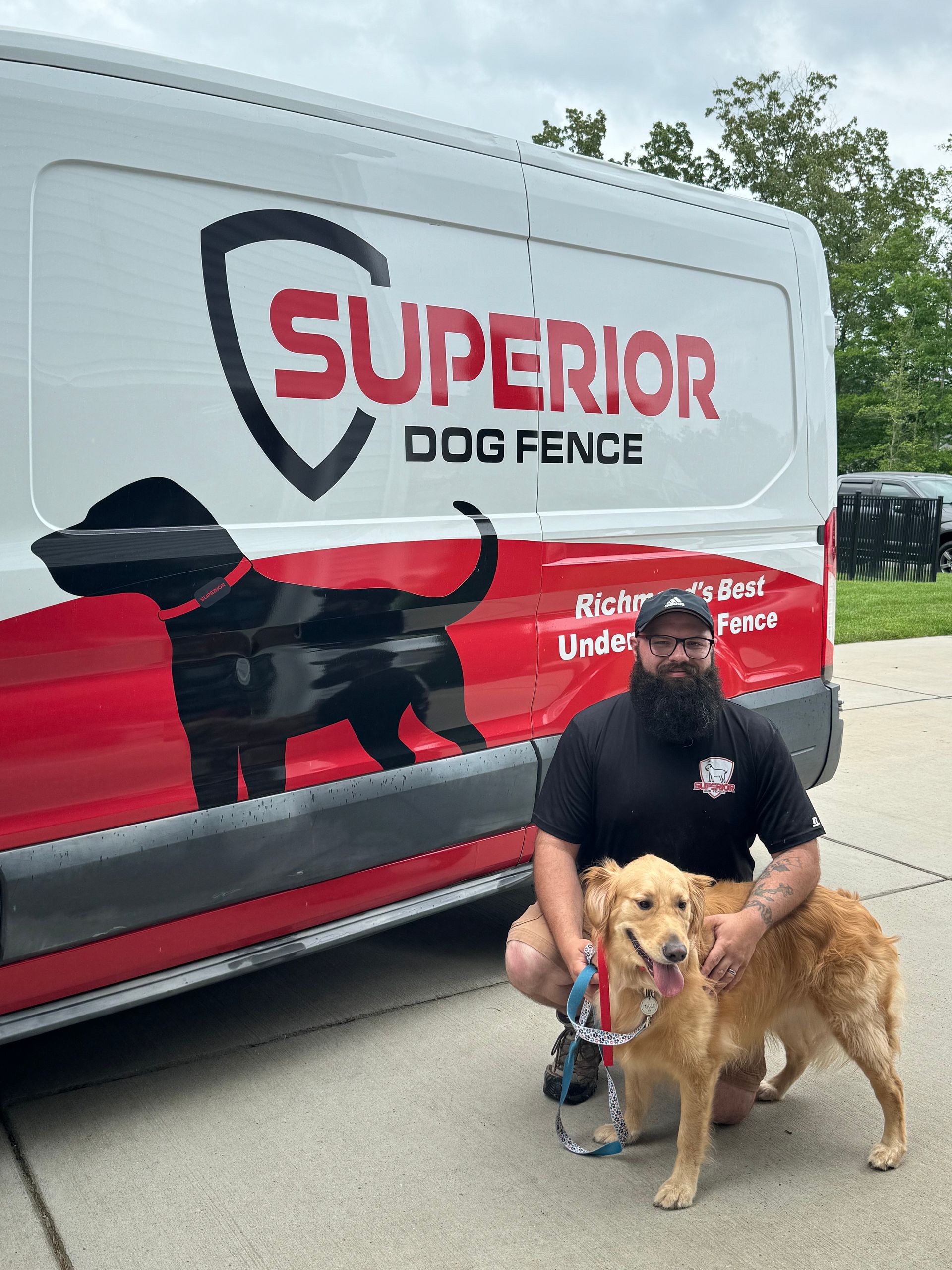 A man is kneeling next to a dog in front of a superior dog fence van.