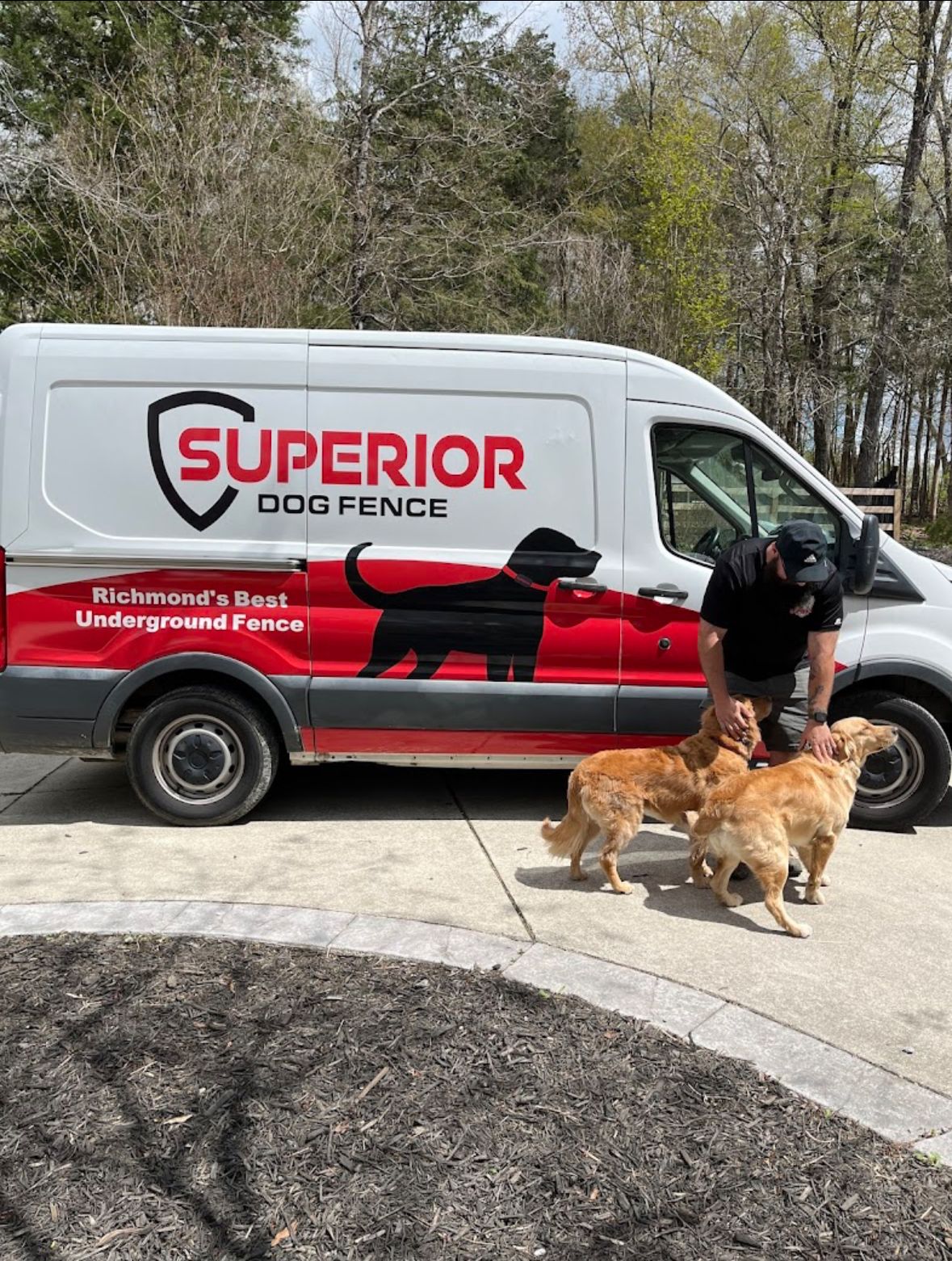 A man is petting three dogs in front of a superior dog fence van.