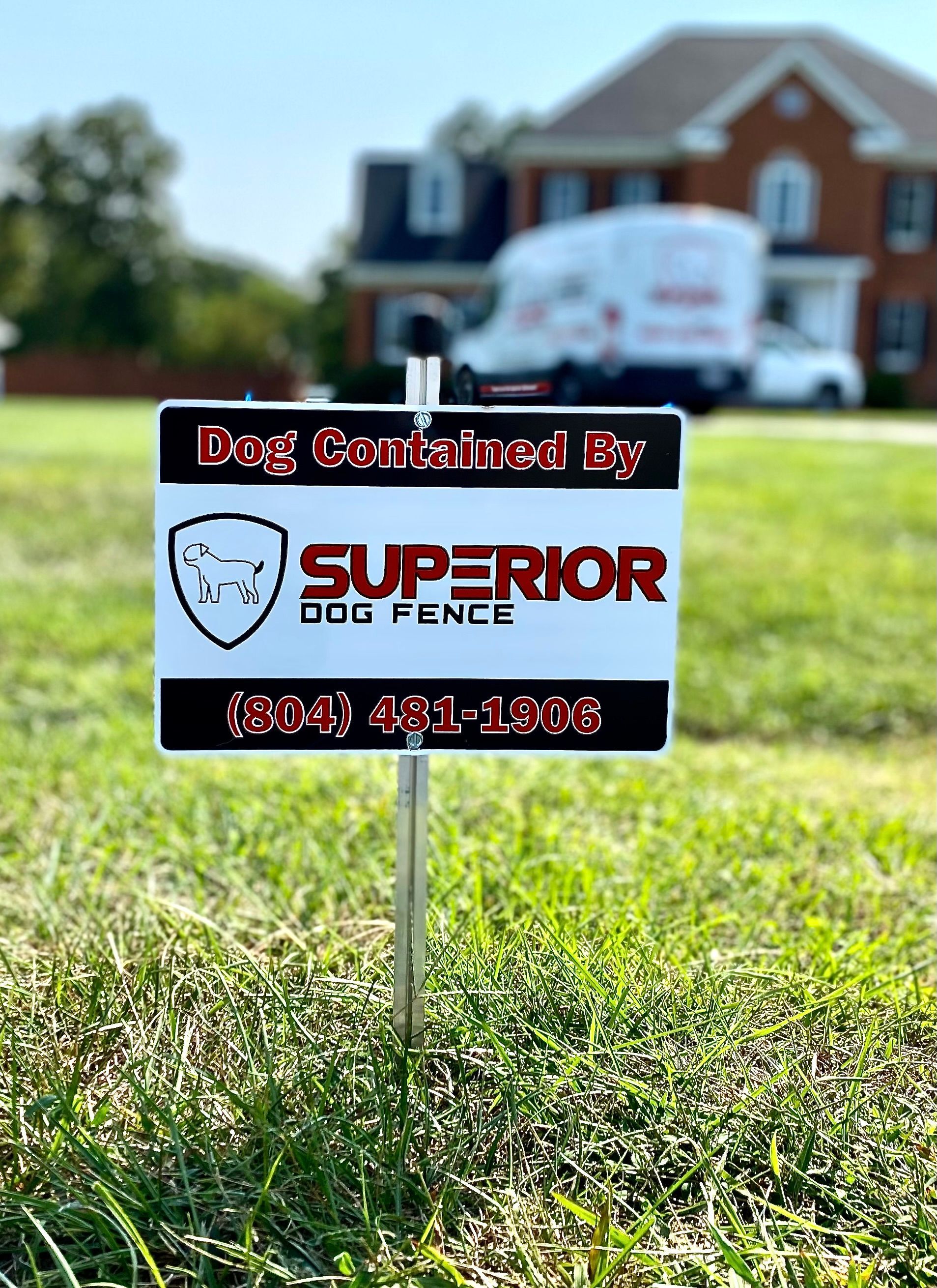 A superior dog fence sign is sitting in the grass in front of a house.