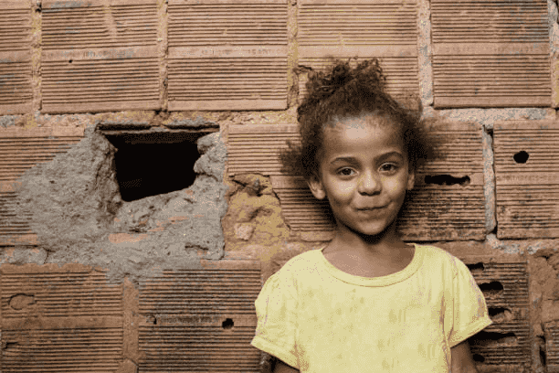 A little girl in a yellow shirt is standing in front of a brick wall.