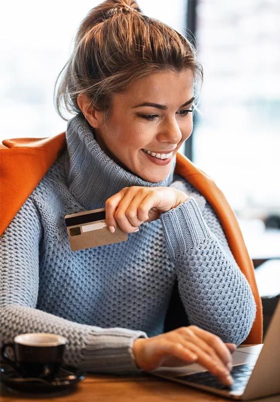 A woman is holding a credit card while using a laptop computer.