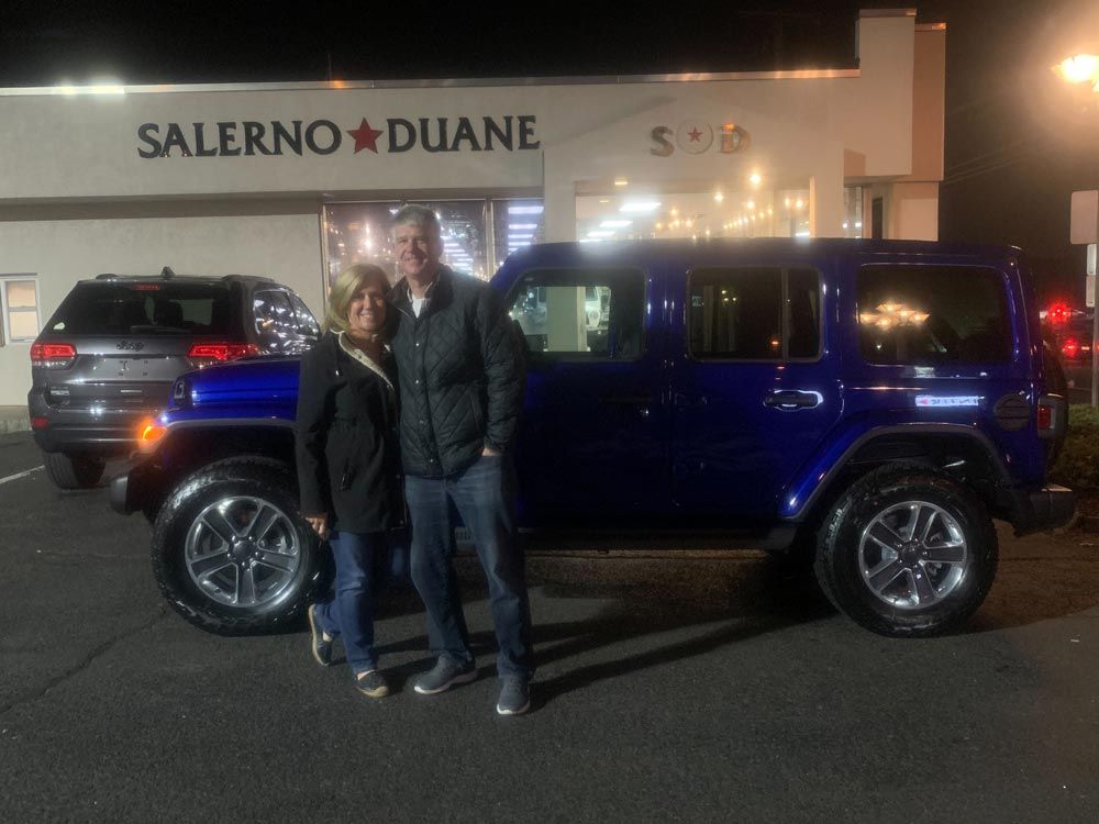 A man and woman are standing in front of a blue jeep.